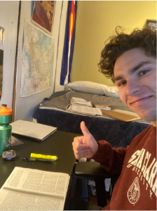 Person smiling and giving a thumbs-up while sitting at a desk with study materials.