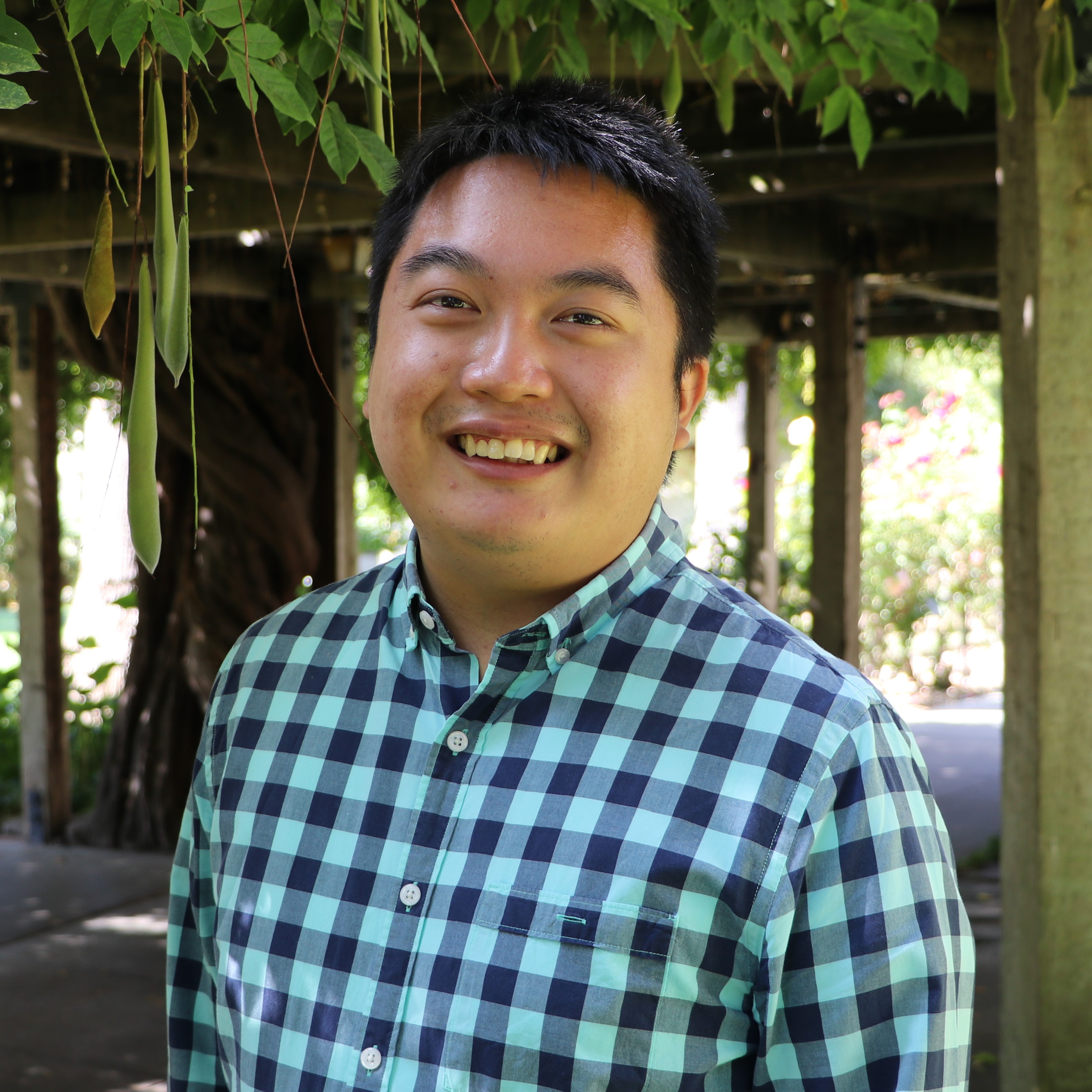 A person in a checkered shirt smiles in an outdoor setting.