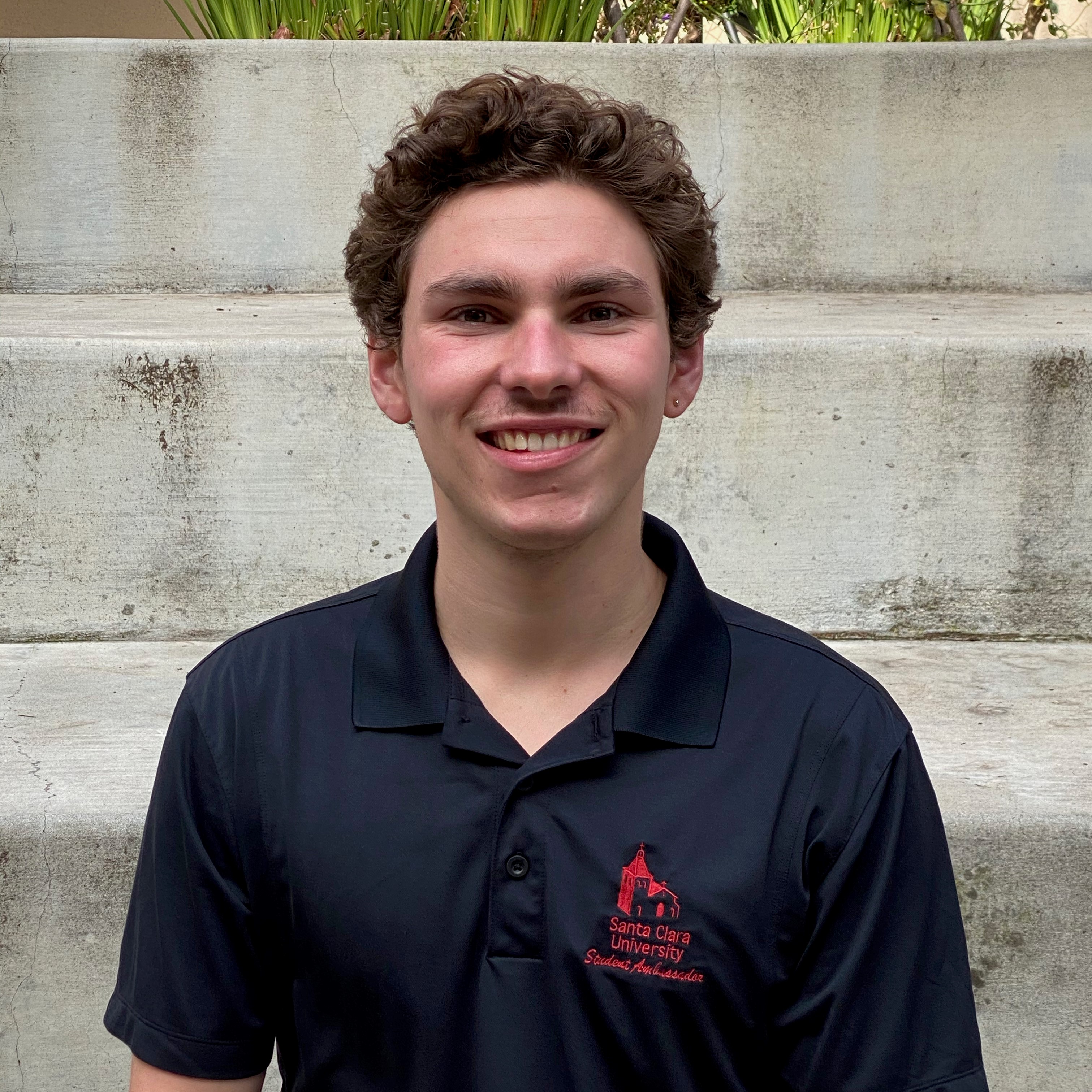 A person in a black shirt with a red logo, standing in front of concrete steps.