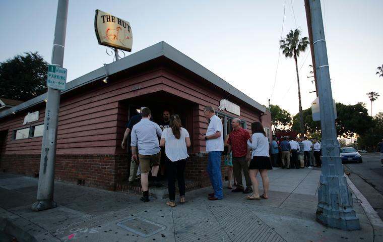 People standing outside a brick building titled The Hut.