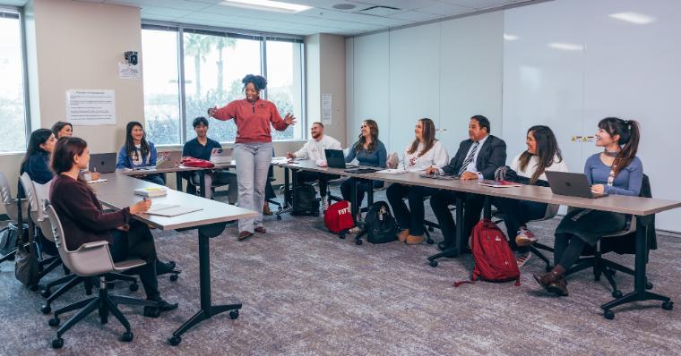 A teacher standing in the center of U-shaped tables with adult students