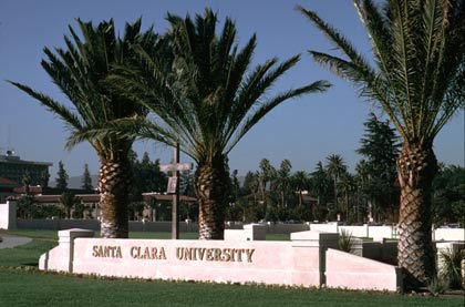 Santa Clara University is written on a sign at campus entrance surrounded by palm trees.