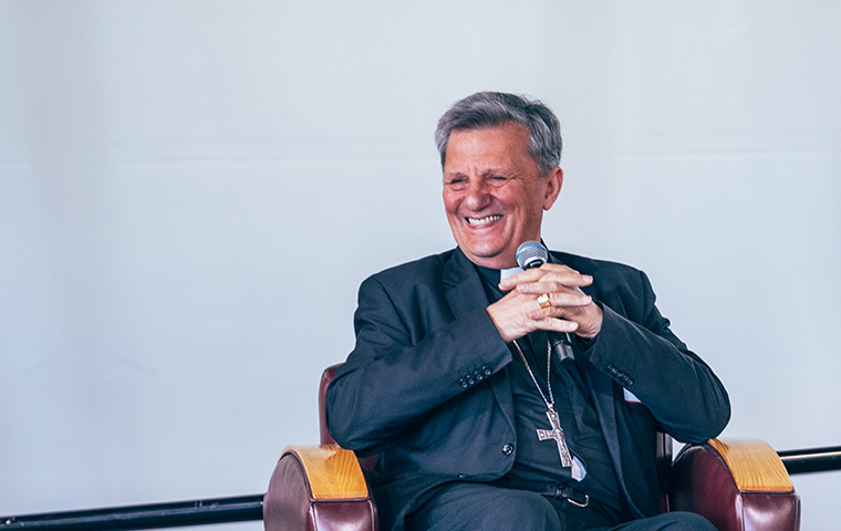Cardinal Mario Grech seated and smiling on stage at Locatelli Center