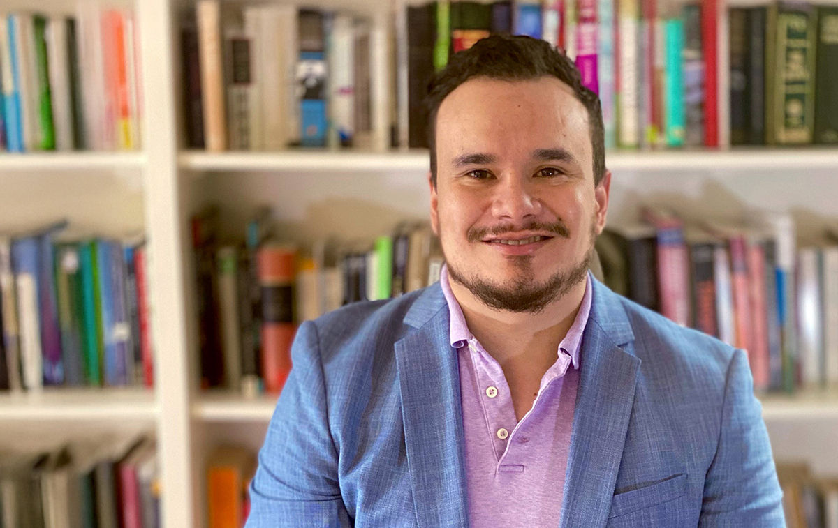 Guadalupe Hayes-Mota sitting in front of book shelf, wearing blue blazer and pink button up.