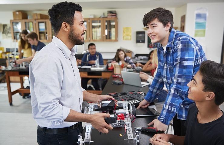 High school students and teacher interacting in STEM classroom.