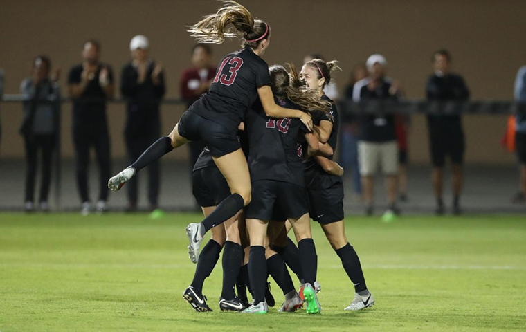 Womens soccer team celebrate in a circle.