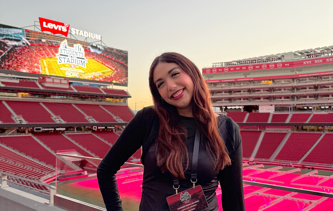 A young Latina woman poses in the 49ers-red Levi's Stadium at dusk.