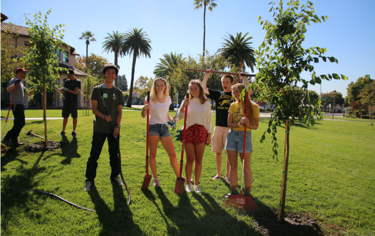 Two students planting a tree in front of Learning Commons