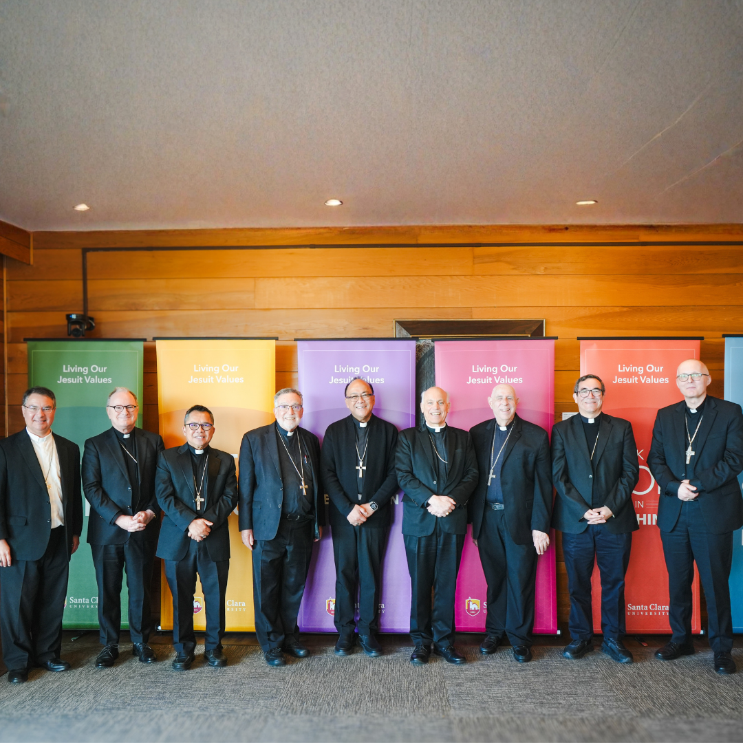 A group of people smiling in front of a wooden wall and colorful banners