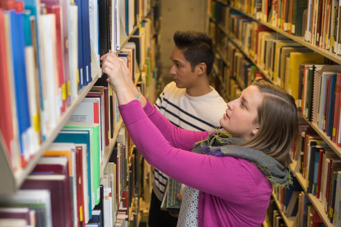 Two people searching bookshelves in a library.