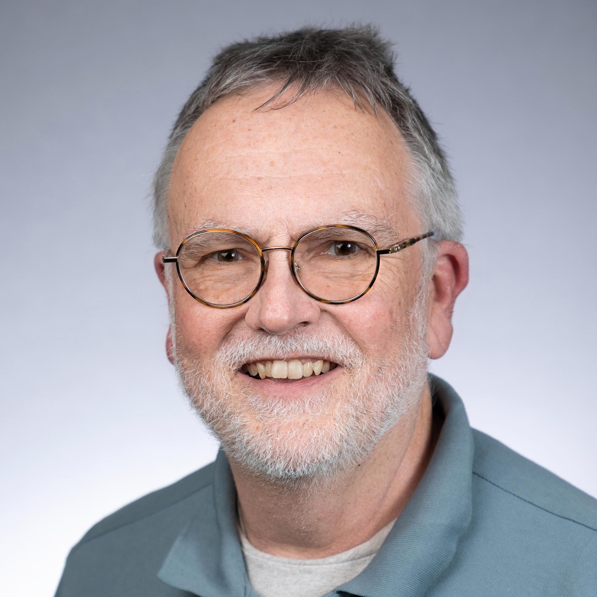 A person wearing glasses and a teal shirt, smiling at the camera.