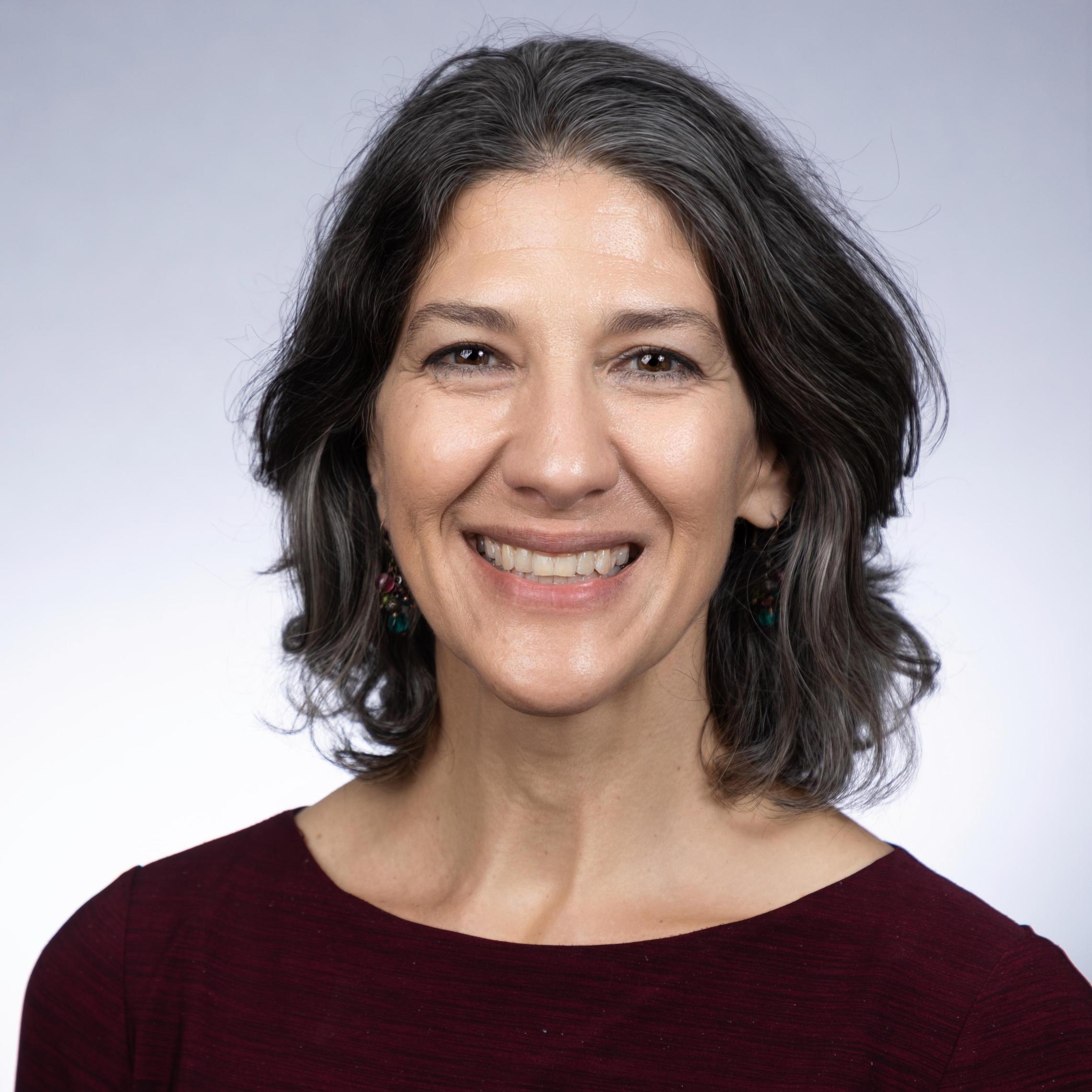 A woman smiling in a headshot with a gray background.