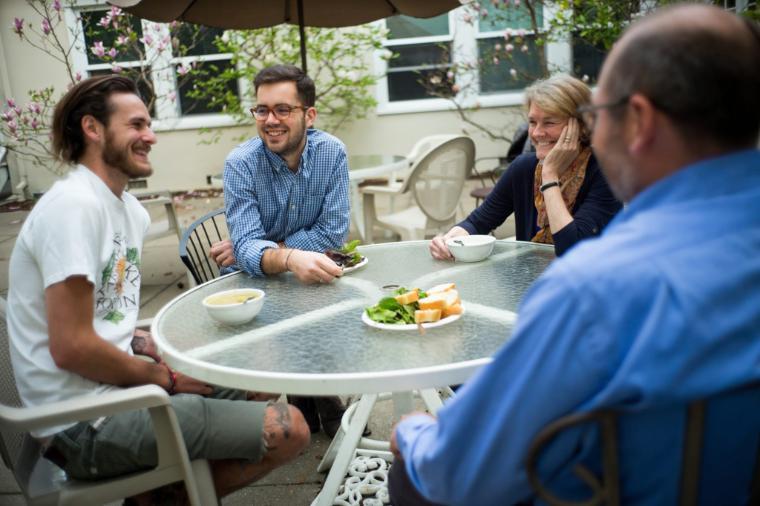 Four people having a meal at a round outdoor table.