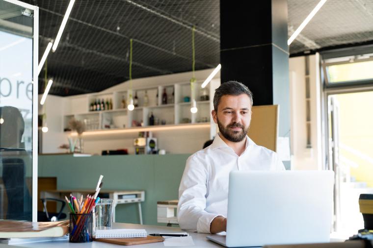 Young businessman working in his office, sitting at the desk, laptop and tablet in front of him