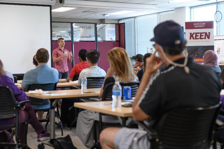 Classroom setting with an instructor speaking to students at desks.