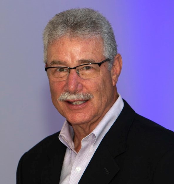 Man in suit with glasses, light mustache, and smiling.