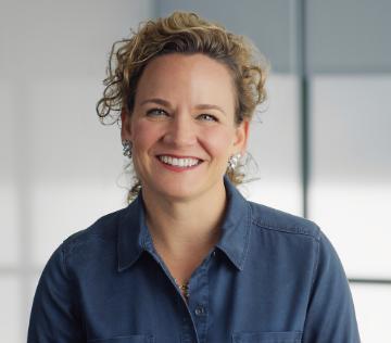 Smiling person in blue shirt posed against a modern office background.