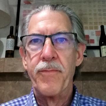 A person wearing glasses in front of shelves with bottles.