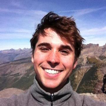 A person smiling with a mountainous landscape in the background.