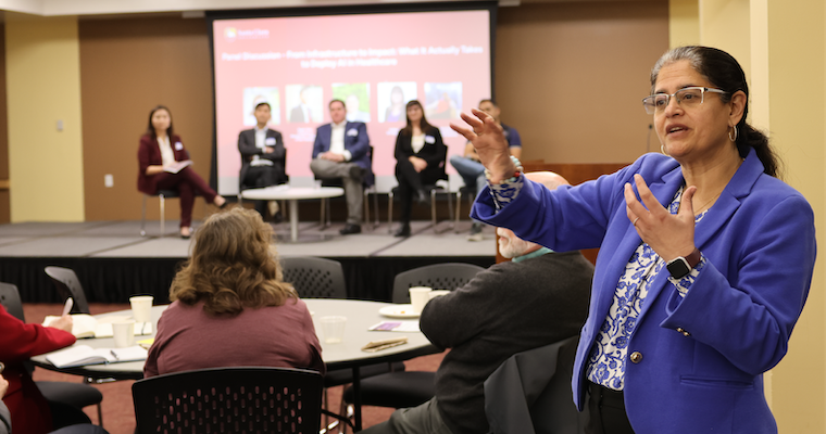 Speaker interacting with the crowd at AI Healthcare Workshop with panelists in the background