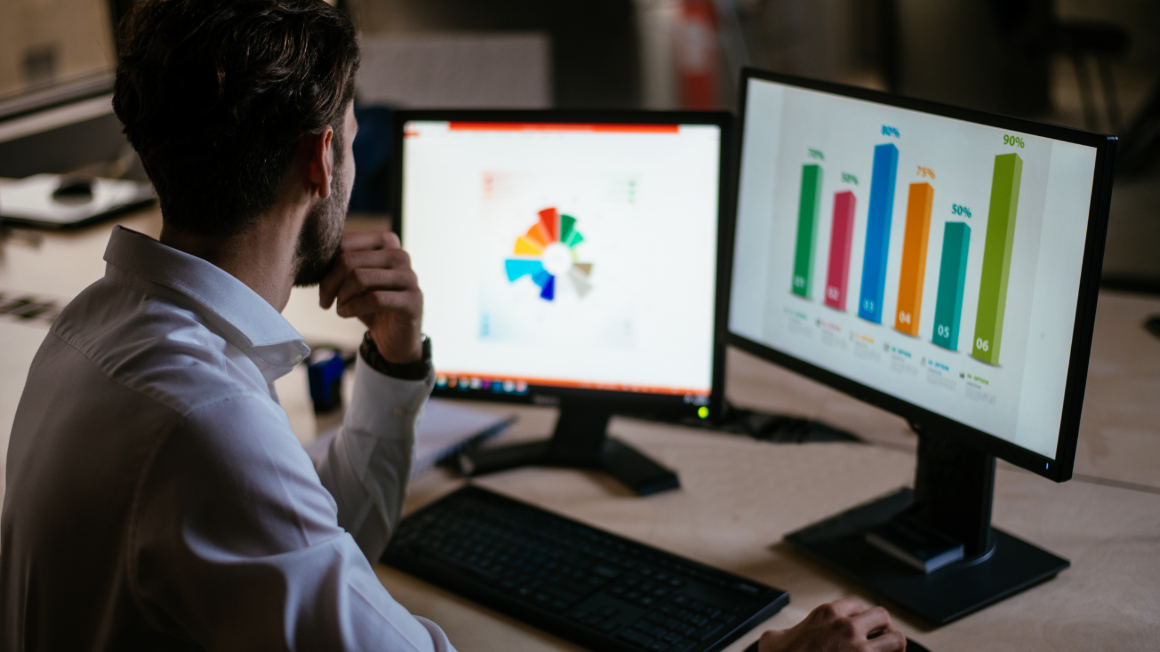 Business professional analyzing colorful graphs on two monitors