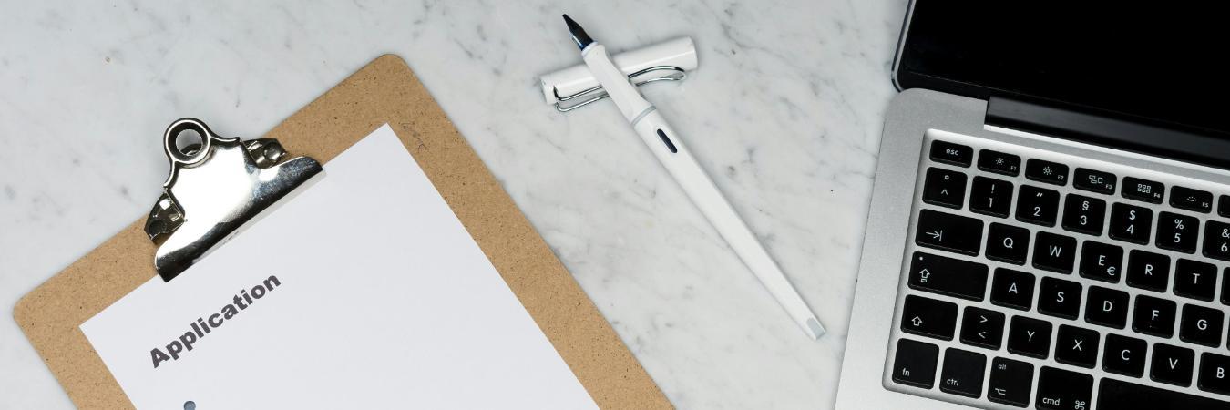 White paper reading 'application' on brown folder beside silver laptop computer