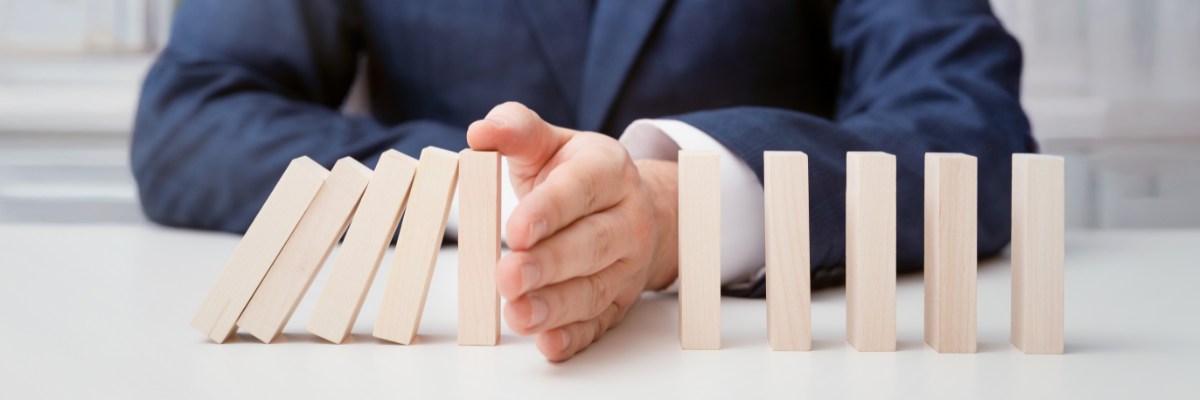 Person in a navy suit uses a hand to stop a row of wooden blocks from falling.