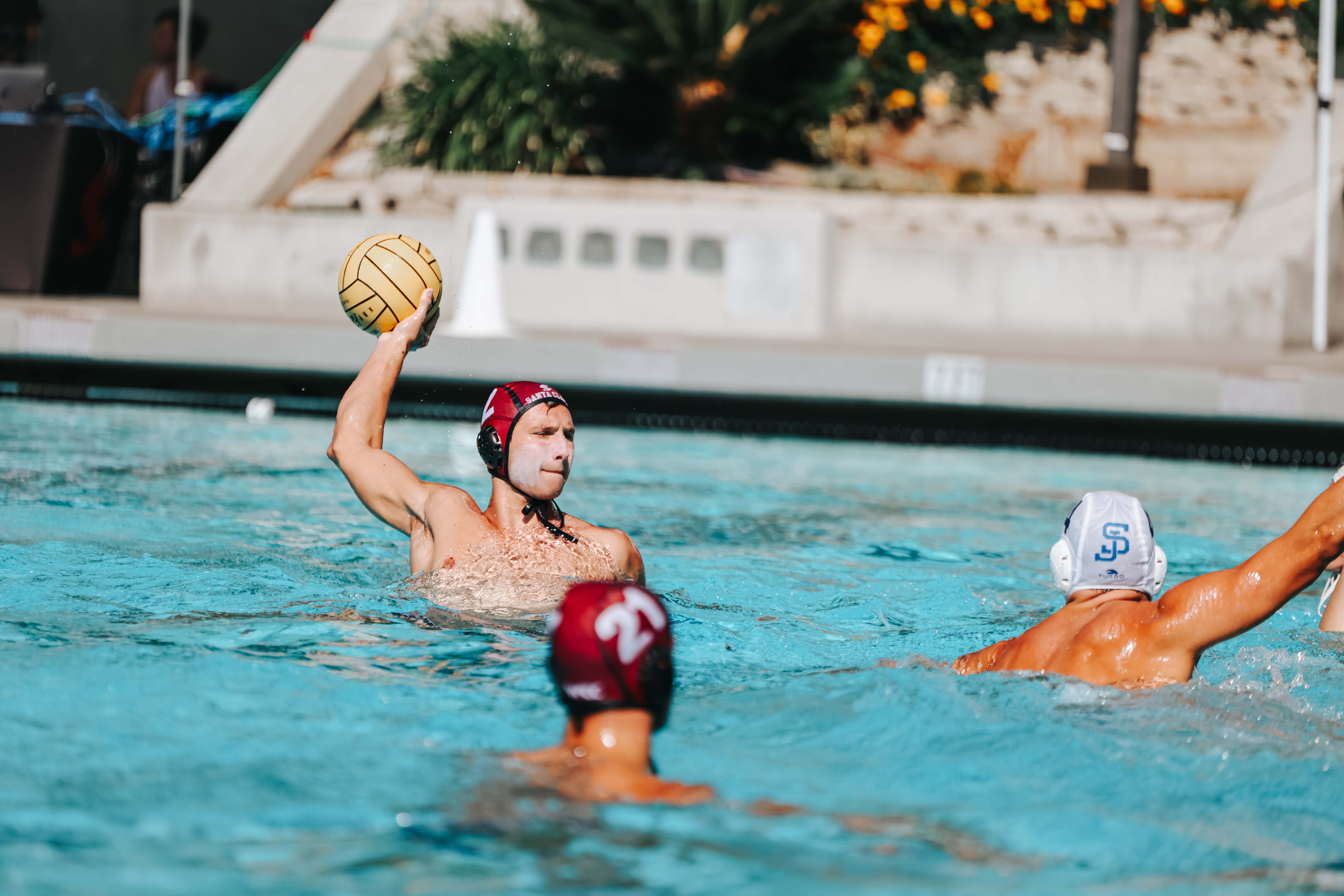 A water polo player treads water with the ball in his right hand, attempting to score over an opponent.