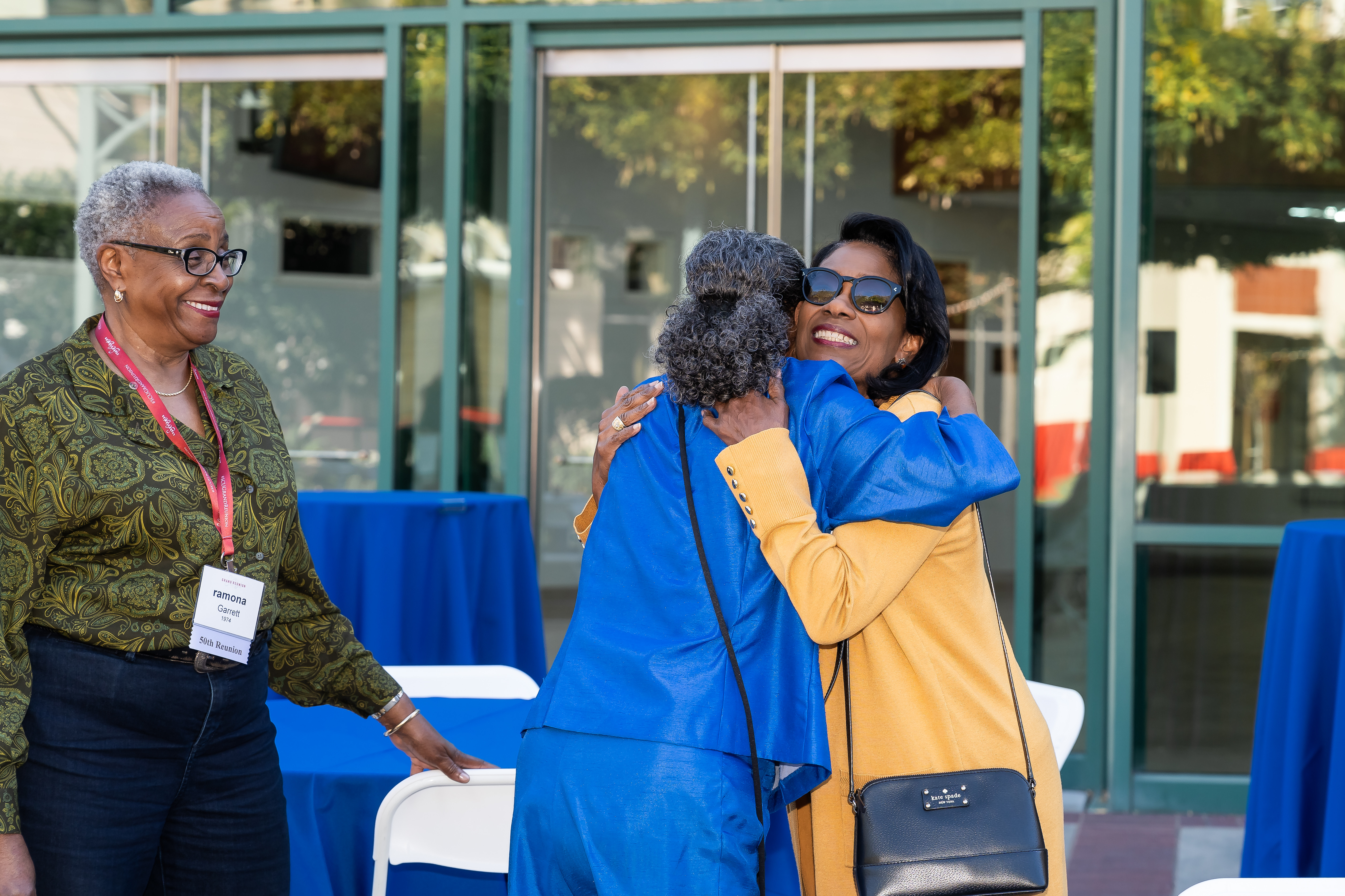 One woman smiles while two other women hug one another