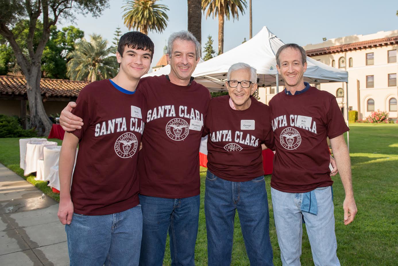 Four people in matching maroon shirts with Handshake printed, standing on a college campus.