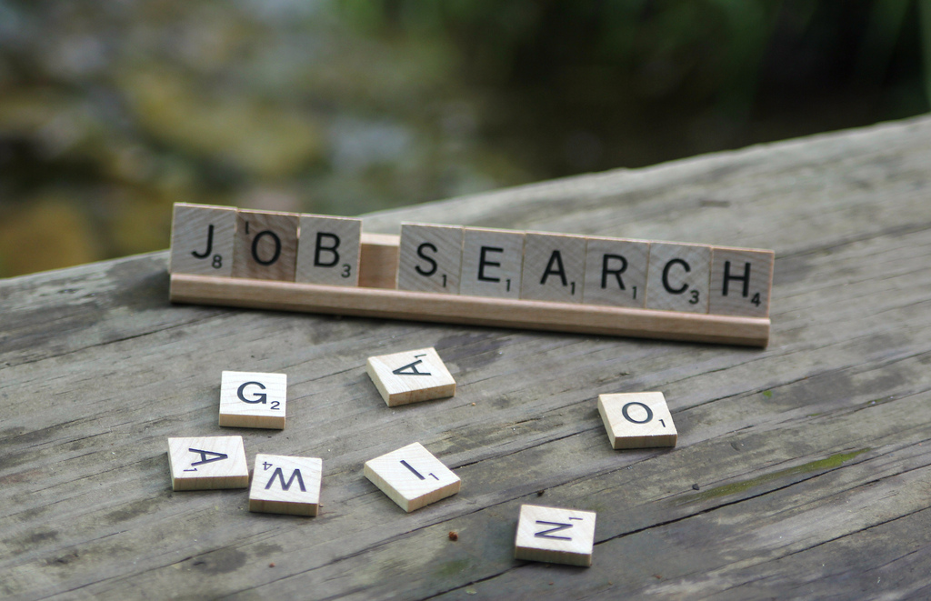 Scrabble tiles spelling “SEARCH JOB” on a wooden surface.