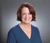 Woman smiling in a headshot with a neutral gray background.