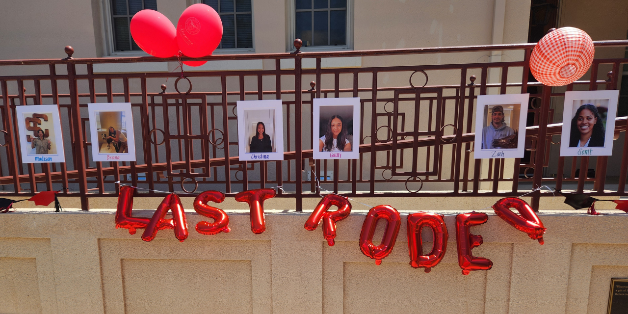 Pictures of several SCU Alumni Association student workers hung up on the metal rails of a walkway. Red and white decor surrounds the photos and red foil balloons hung up underneath the photos read Last Rodeo.