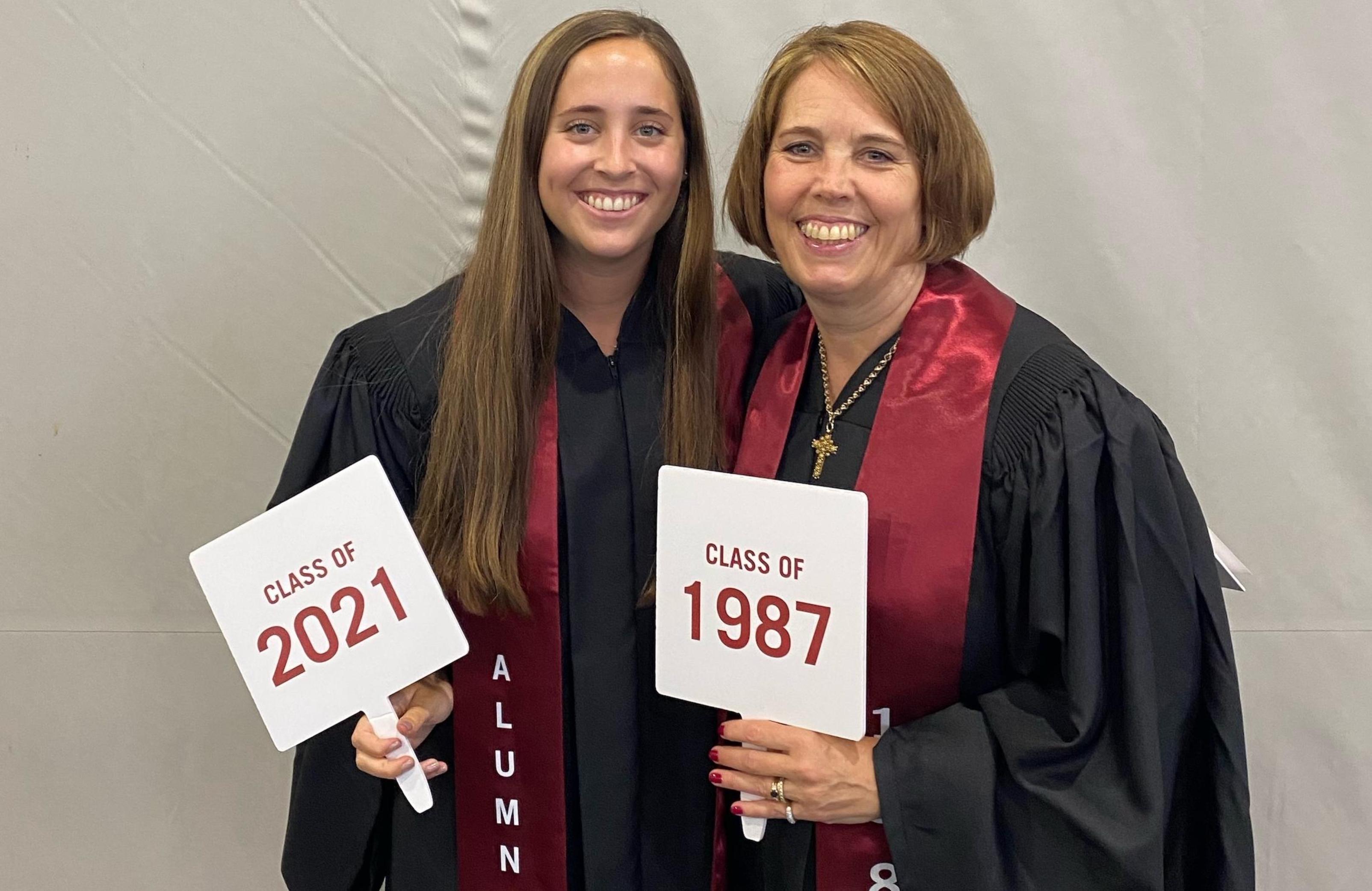 Two people in graduation gowns holding diplomas and smiling.