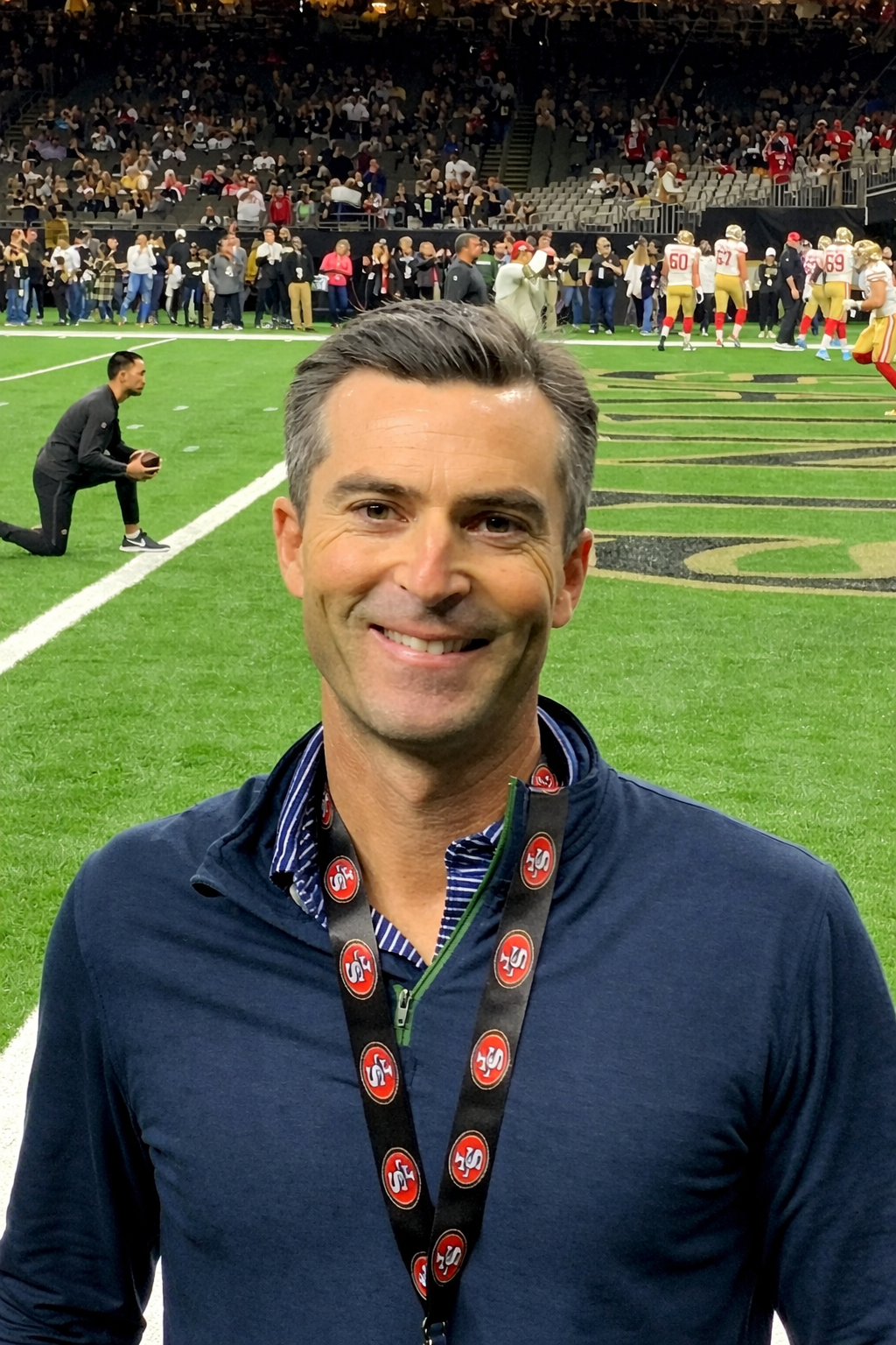 A smiling man wearing a San Francisco Giants lanyard and standing in front of a football field.