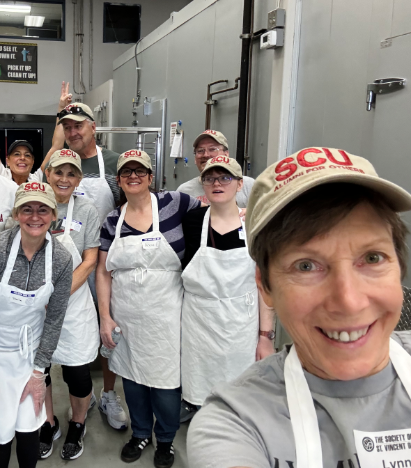 Selfie of a group of volunteers in white aprons and tan SCU hats
