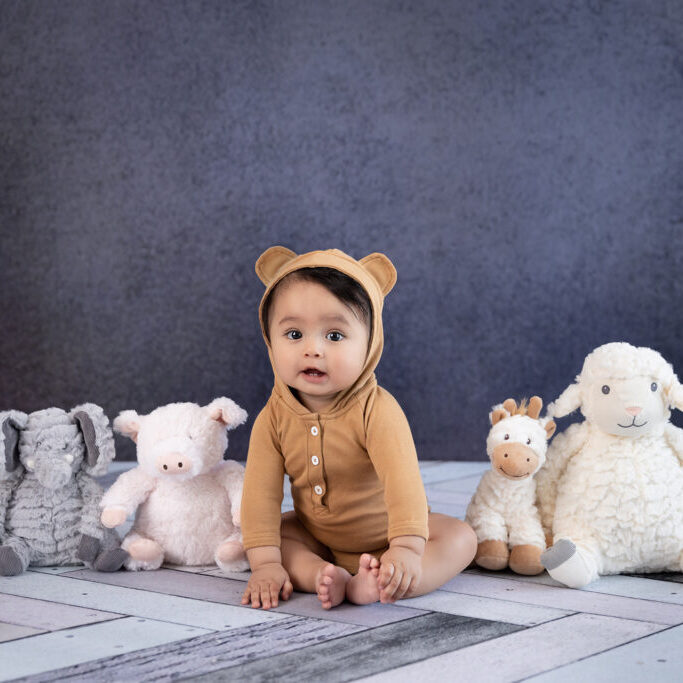 A baby in a bear costume sits with stuffed animals.