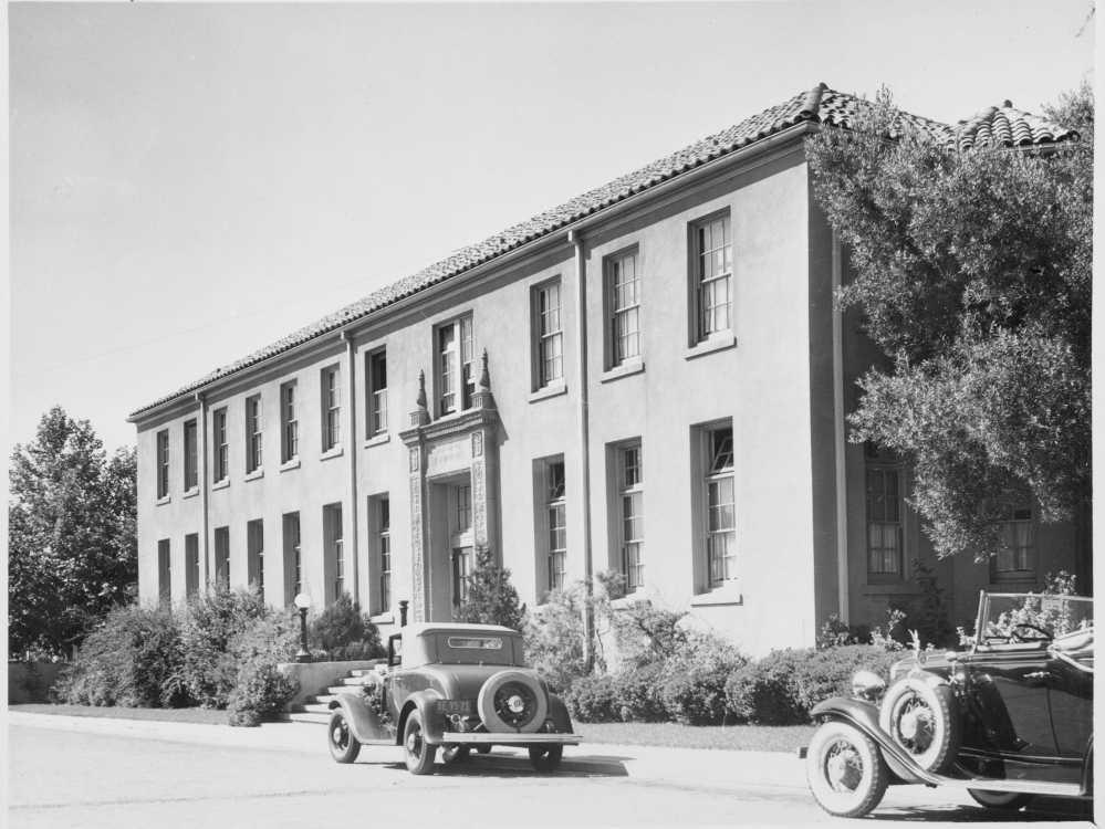 Black and white image of the Donohoe Infirmary with cars driving in front of it