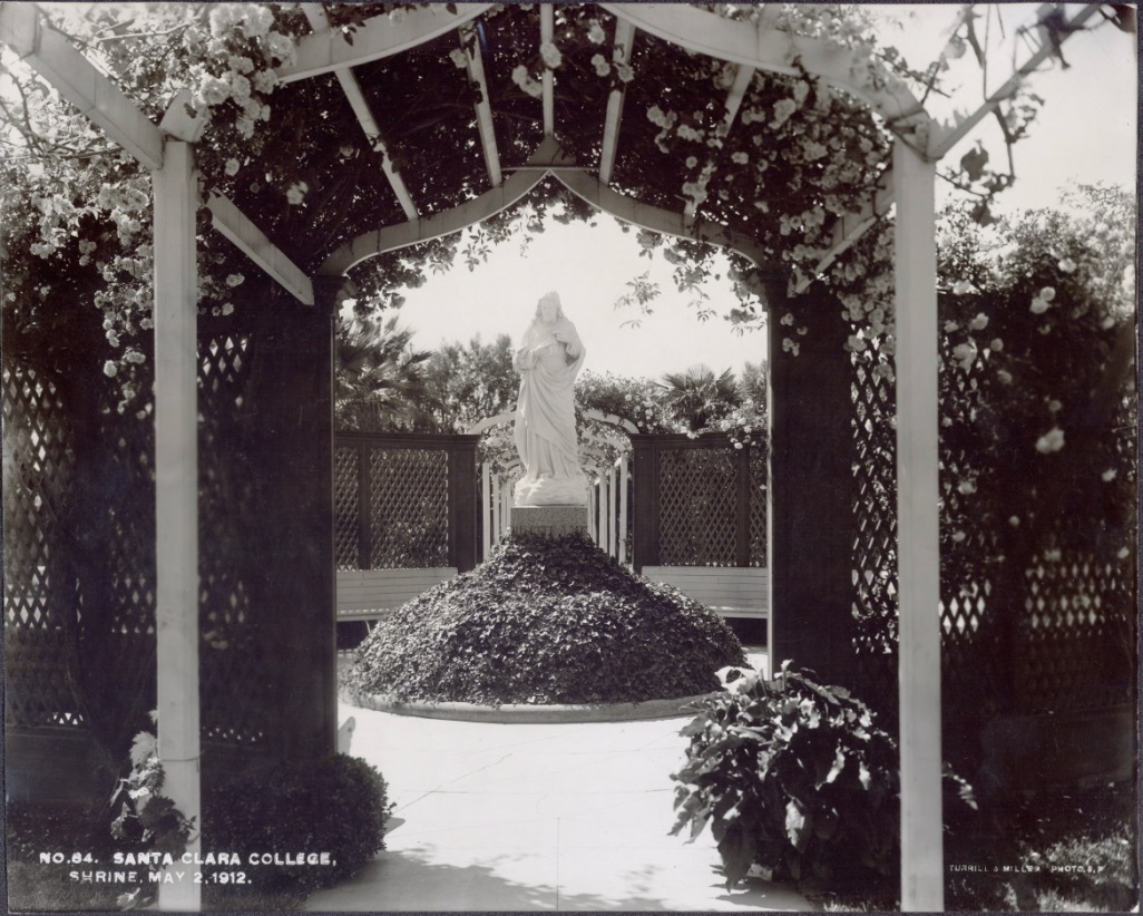 Statue of the Sacred Heart under an arch in a garden.