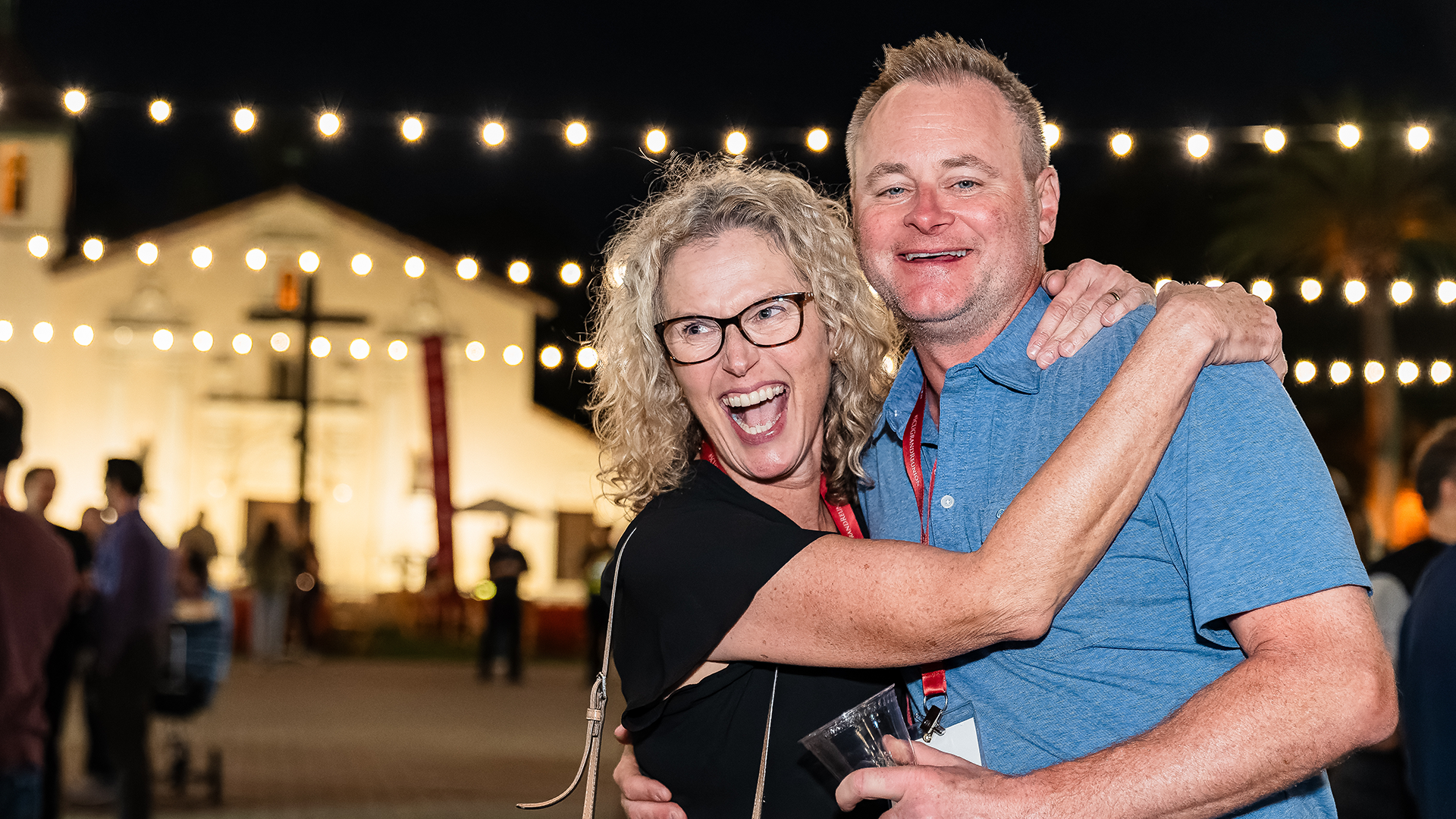 Two alumni smiling broadly with Mission Santa Clara in the background