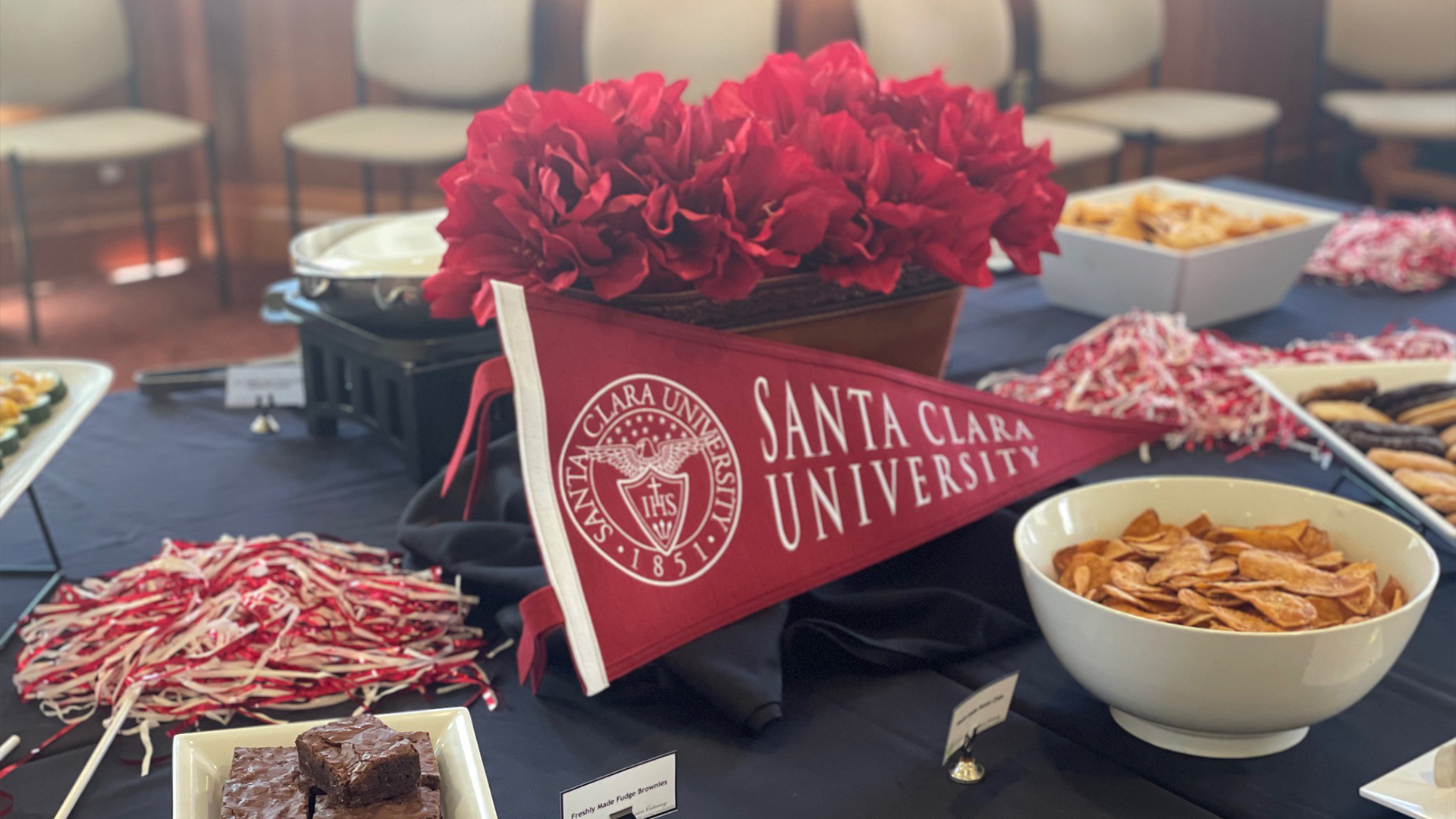 An SCU pennant amongst red carnations, pom poms, and a desserts buffet