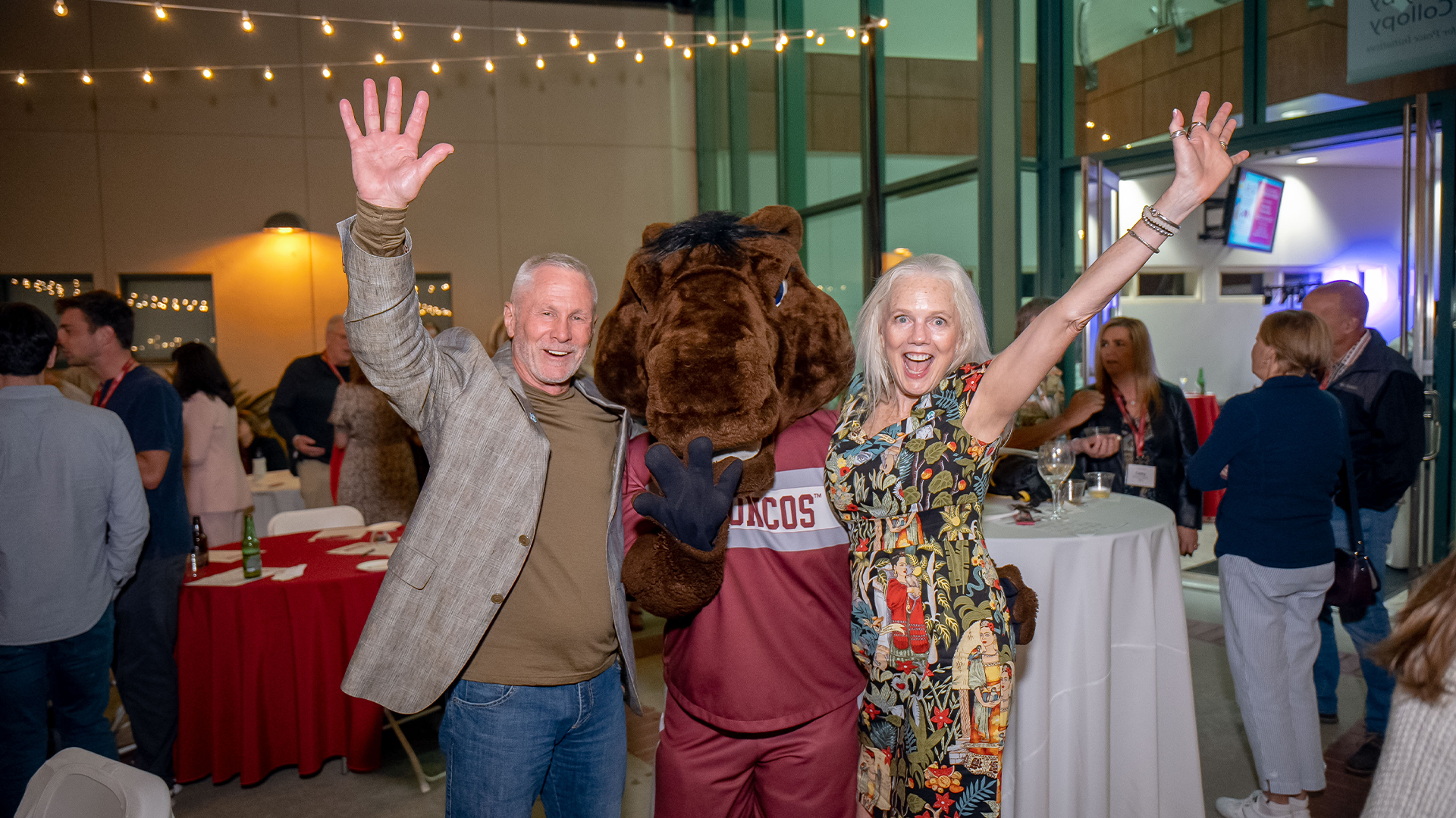 Two alumni throw their hands up with Bucky Bronco