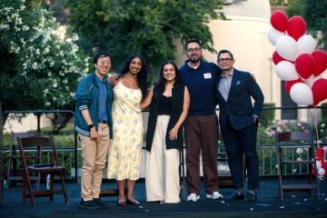 Five people smiling and posing for a photo in front of a red and white balloon column.