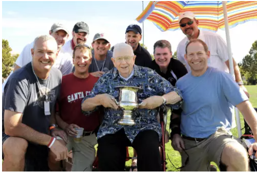 A group of people outdoors; one holding a rugby trophy.