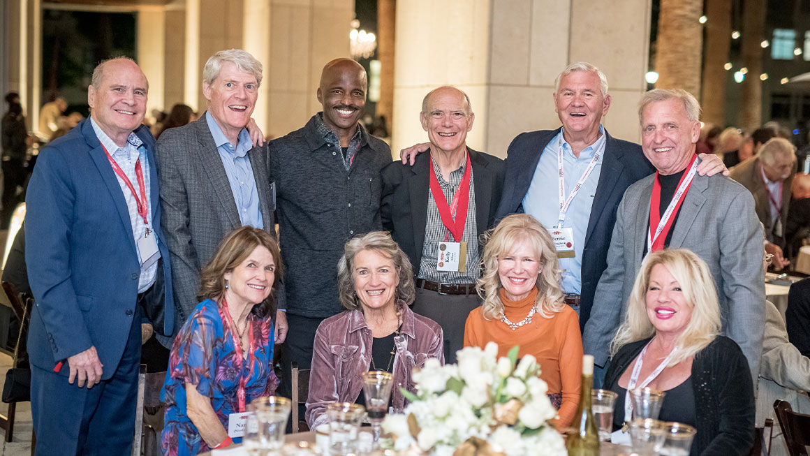 A large group of people sitting around a table and smiling at the camera 