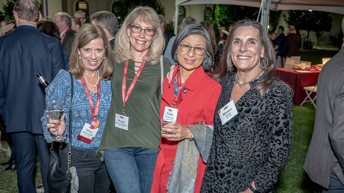 Four women standing arm-in-arm and smiling at the camera 