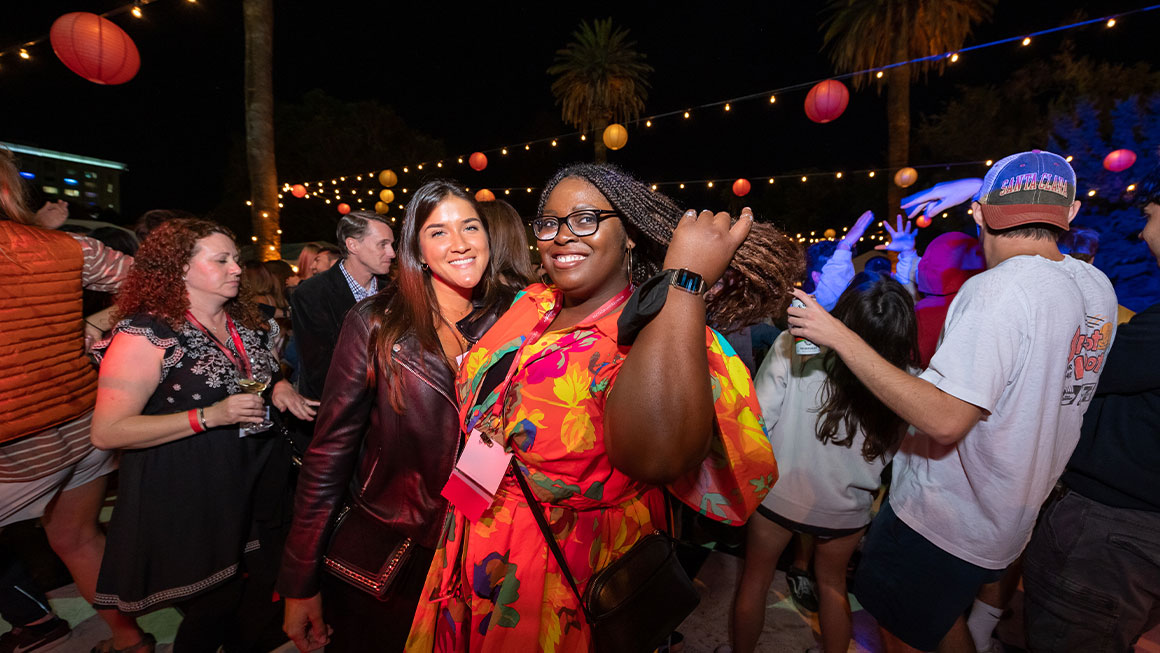 Two women smiling at the camera in the midst of a group of dancers 