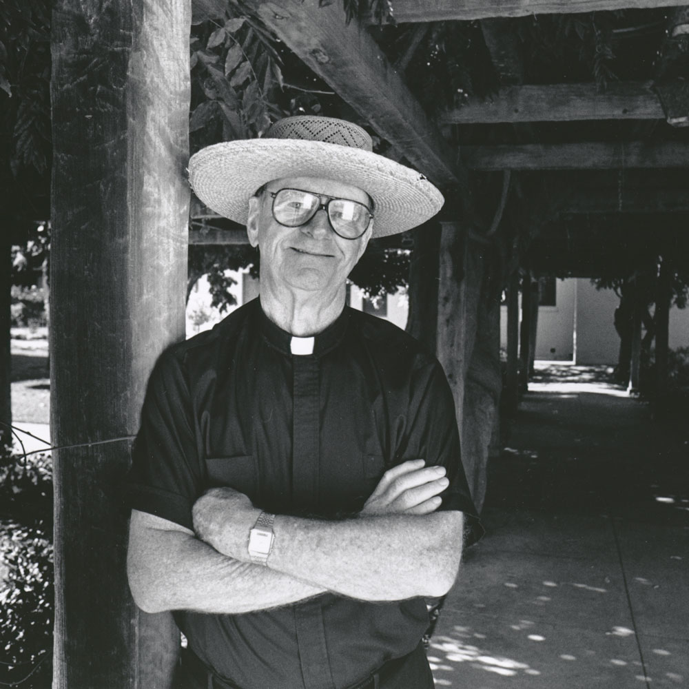 A mean in a straw hat leans against a pillar in the Mission Gardens