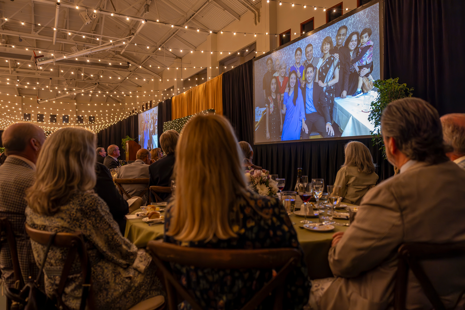 A large group of people watches a video playing on two screens