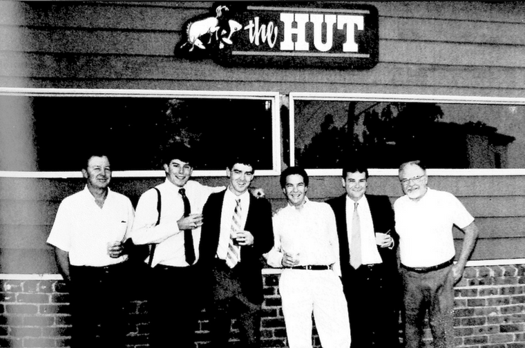 Six people standing outside a building with Hut sign.